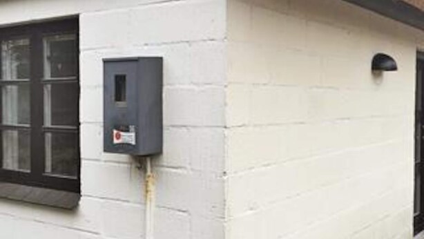 Fachada de edificio con ventana, puerta y un cuadro eléctrico en la pared.