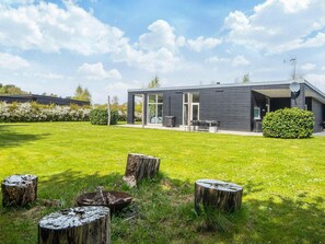 A modern house with a large glass door, a satellite dish, and a well-maintained lawn with wooden stumps.