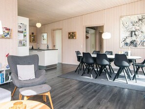 A modern living room with a grey armchair, a dining table with black chairs, a kitchen area, and a large abstract painting on the wall.