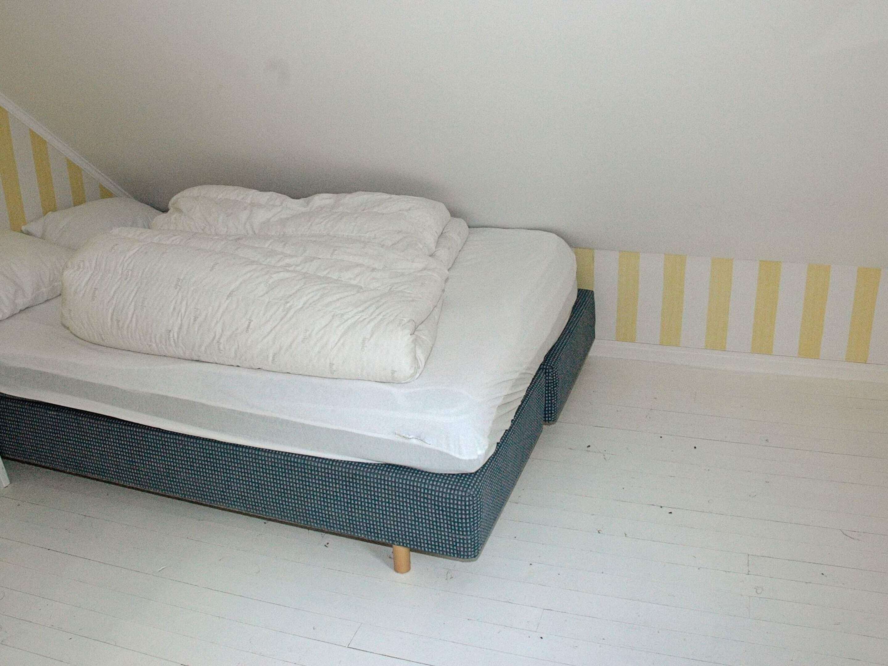 A bed with a white mattress and pillows, a green upholstered headboard, and a white wall with yellow stripes.