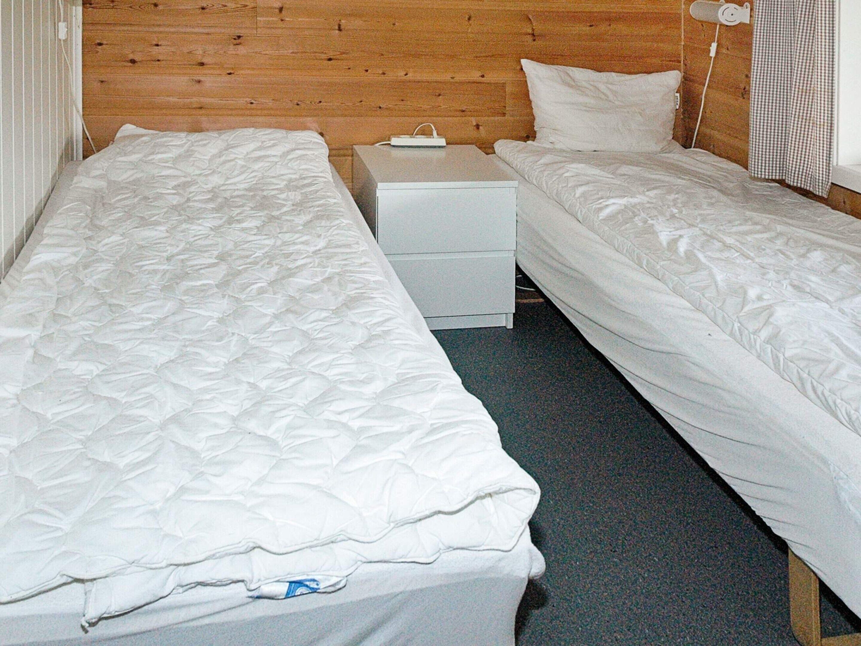 A room with two single beds, a small bedside table, and a wall-mounted nightstand.