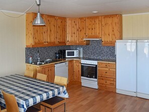 A compact kitchen with wooden cabinets, a microwave, a stove, and a refrigerator. - 4 Star Holiday Home in Aukra (Aukra)