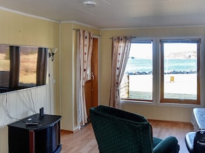 A room with a television, a desk, a chair, and a view of the sea through large windows. - 4 Star Holiday Home in Aukra (Aukra)