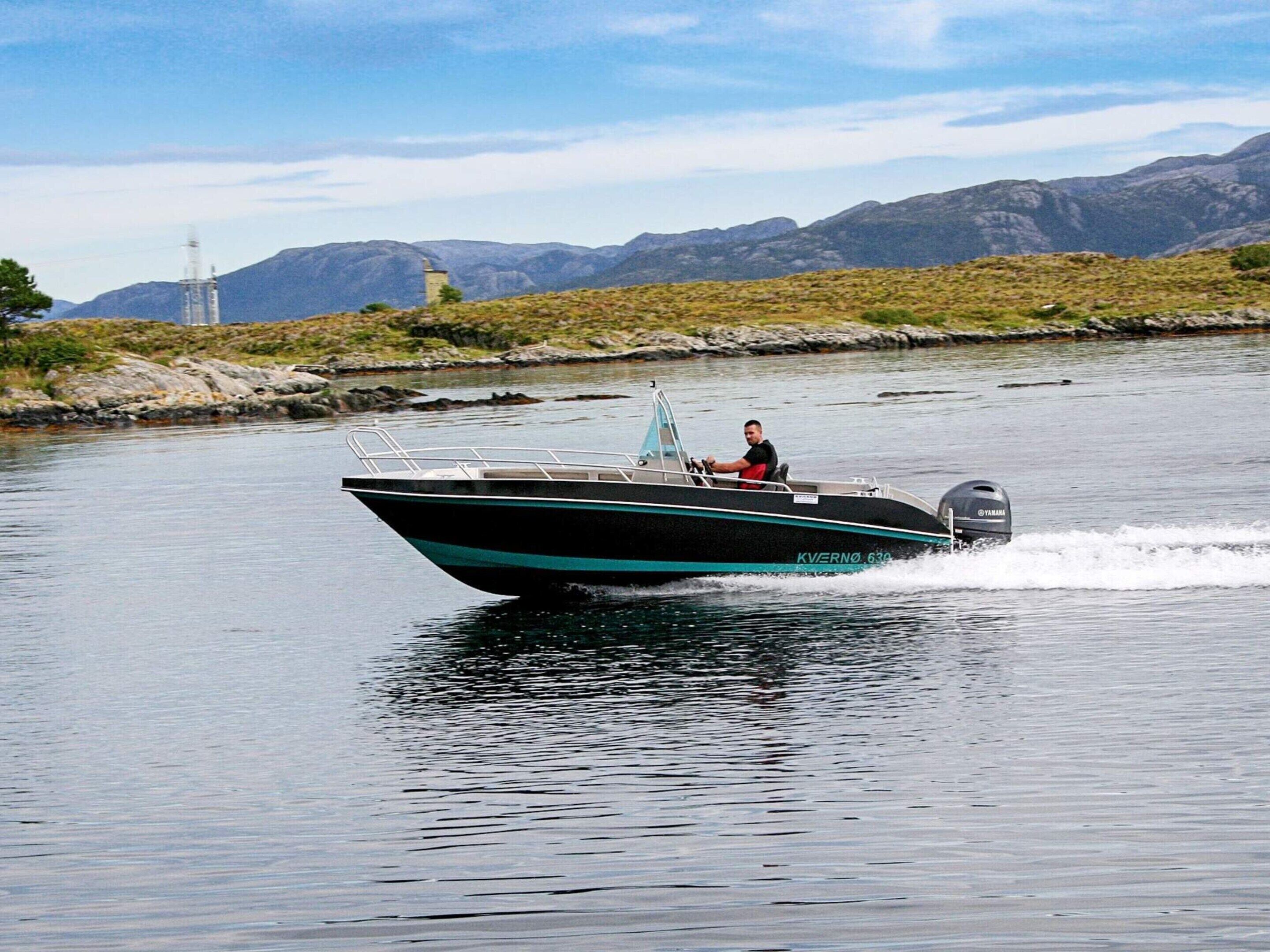 A motorboat on a calm body of water with a mountainous landscape in the background.