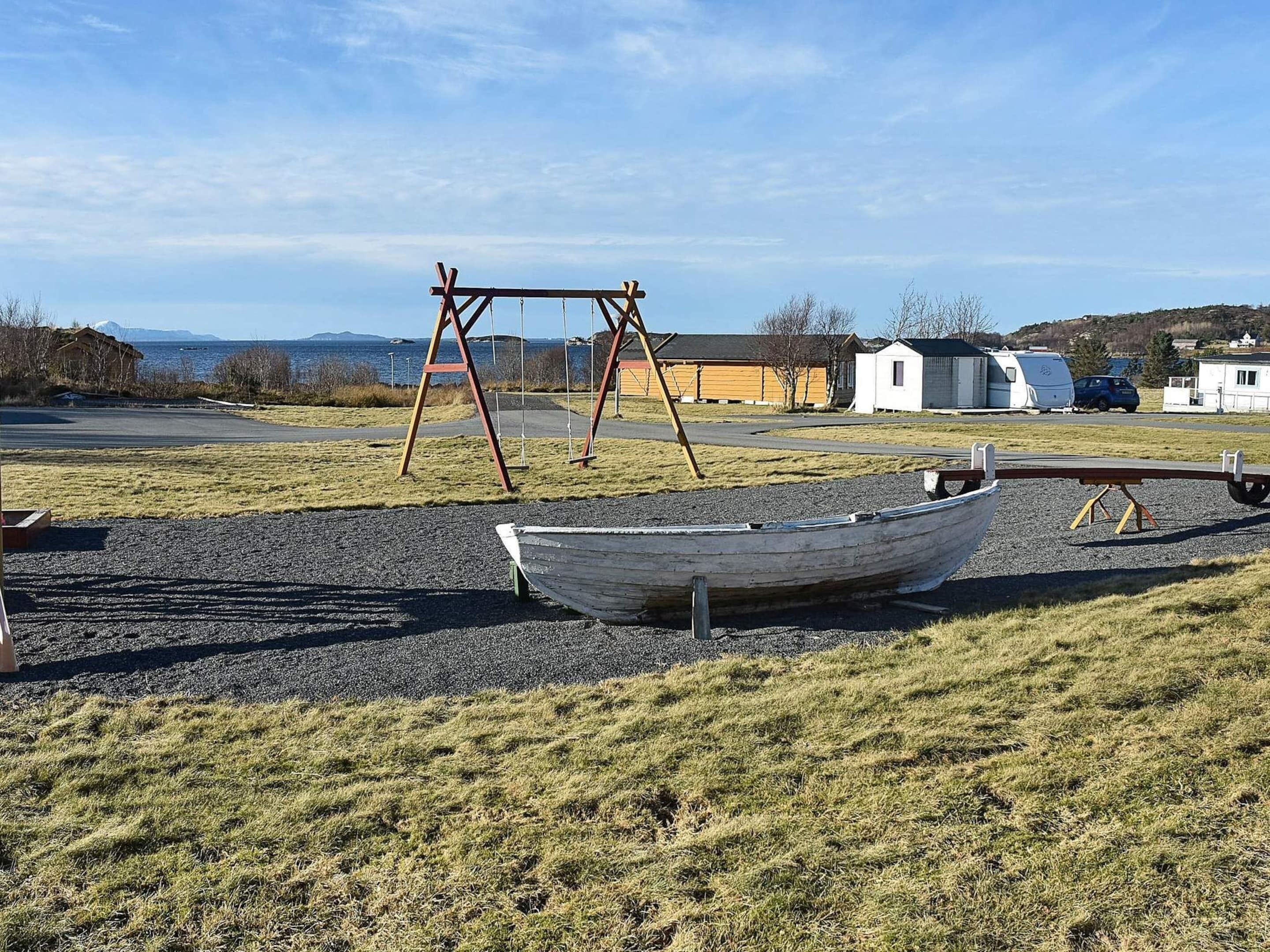 A boat on a gravel area with a swing set in the background.