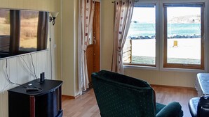 A room with a television, a desk, a chair, and a view of the sea through large windows. - 4 Star Holiday Home in Aukra (Aukra)