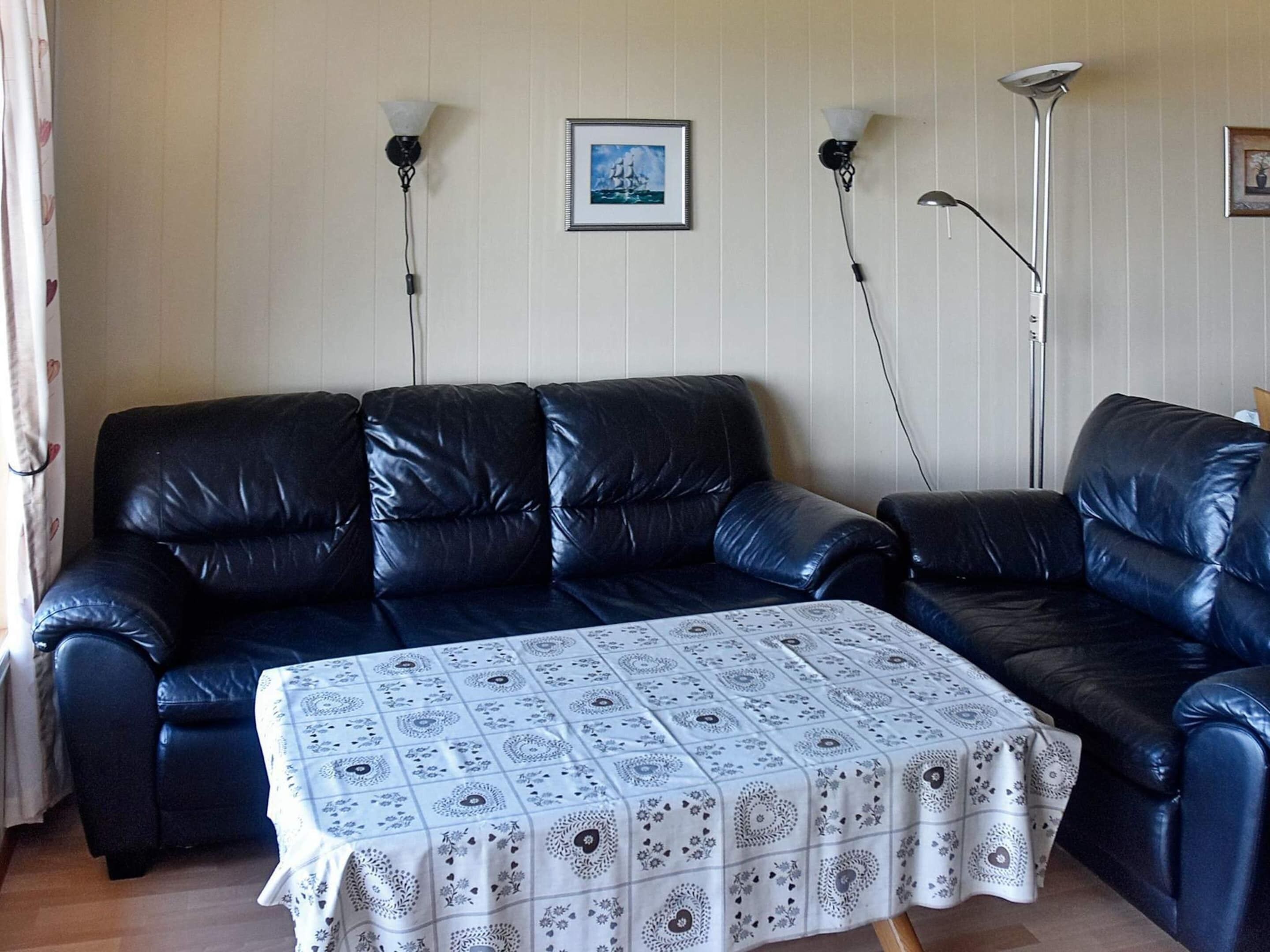 A living room with a black leather sofa, a patterned table, and two wall-mounted lamps.
