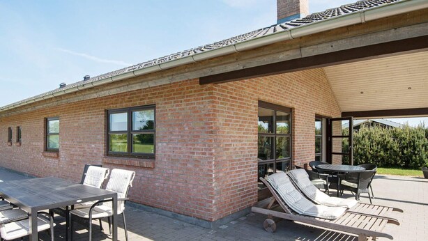 A patio with a brick wall, a table, chairs, and a sun lounger. - 8 Person Holiday Home in Sydals-by Traum (Sydals)