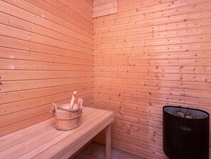 A sauna room with wooden walls, a bench, and a black trash bin.