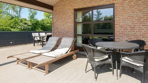 An outdoor patio with lounge chairs and a table, a brick wall, and a large window. - 8 Person Holiday Home in Sydals-by Traum (Sydals)