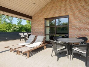 An outdoor patio with lounge chairs and a table, a brick wall, and a large window.