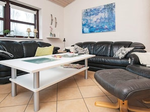 A living room with a black leather sofa, a white coffee table, and a large painting on the wall.