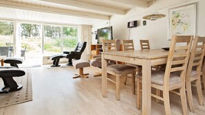 Un'ampia zona giorno con tavolo da pranzo in legno, comodi posti a sedere, televisione a schermo piatto e ampie finestre con vista sull'esterno.