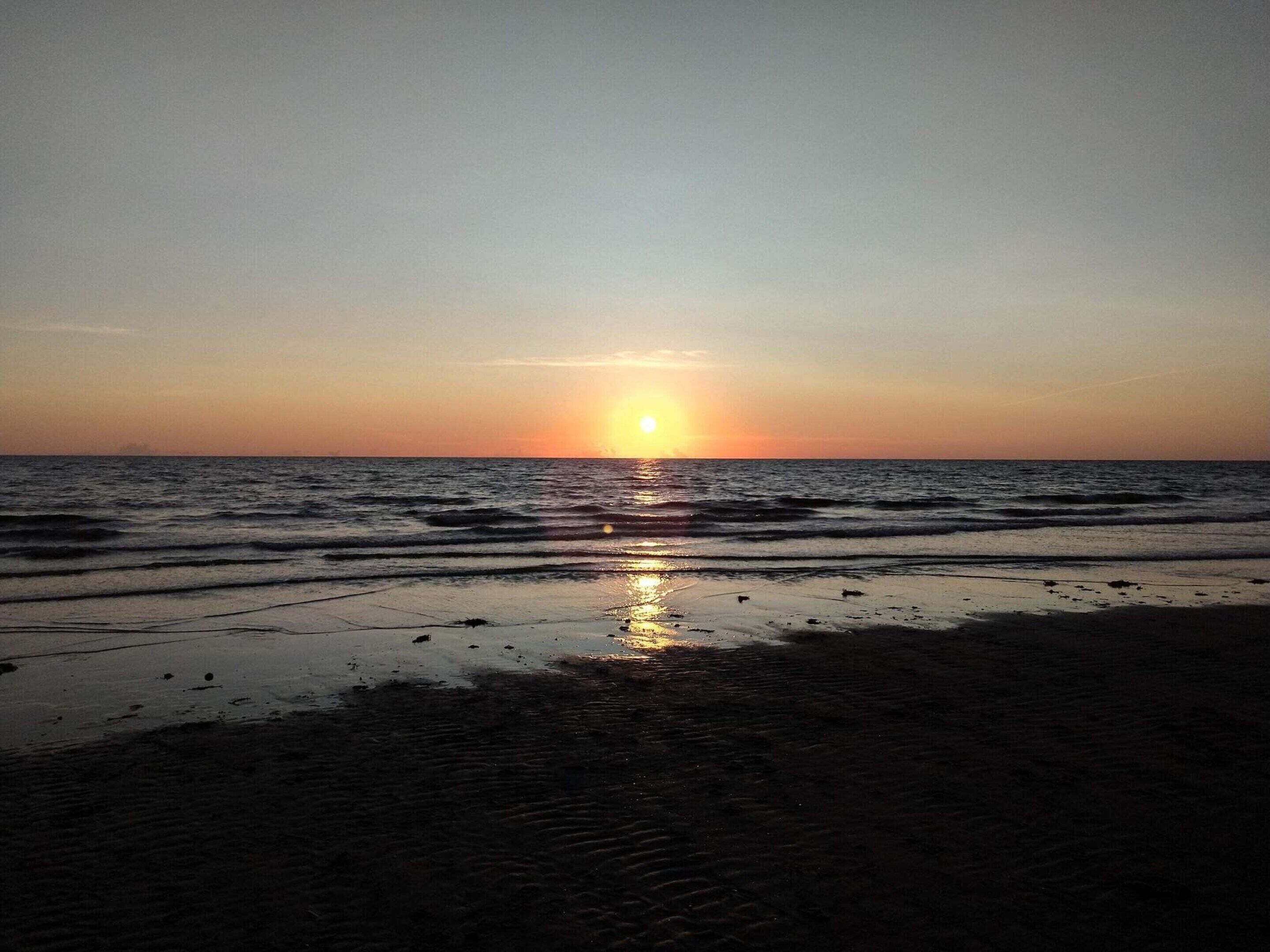 Escena de playa con el sol poniéndose sobre el océano.