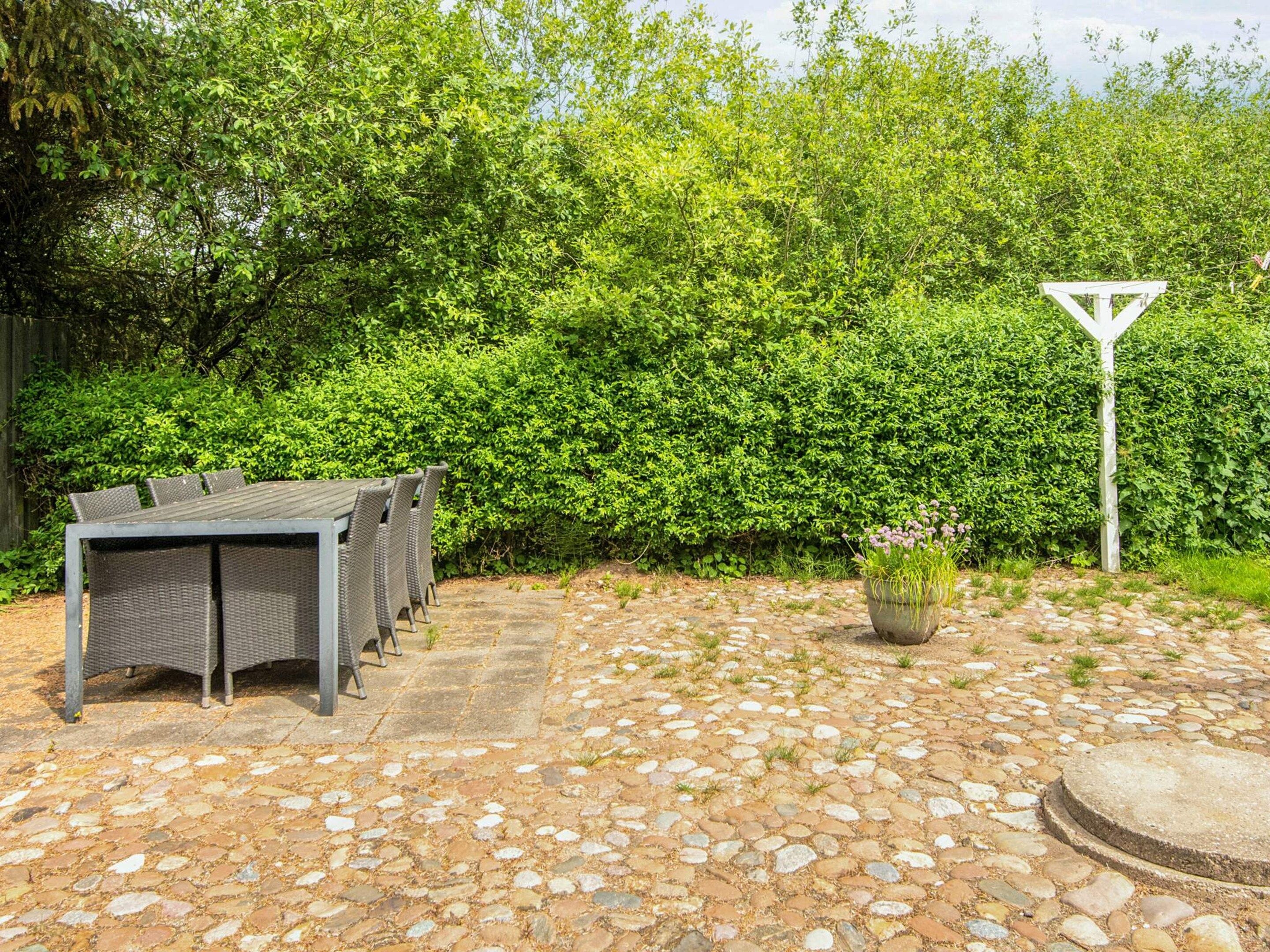 Een terras buiten met een stenen vloer, een tafel met stoelen en een haag op de achtergrond.