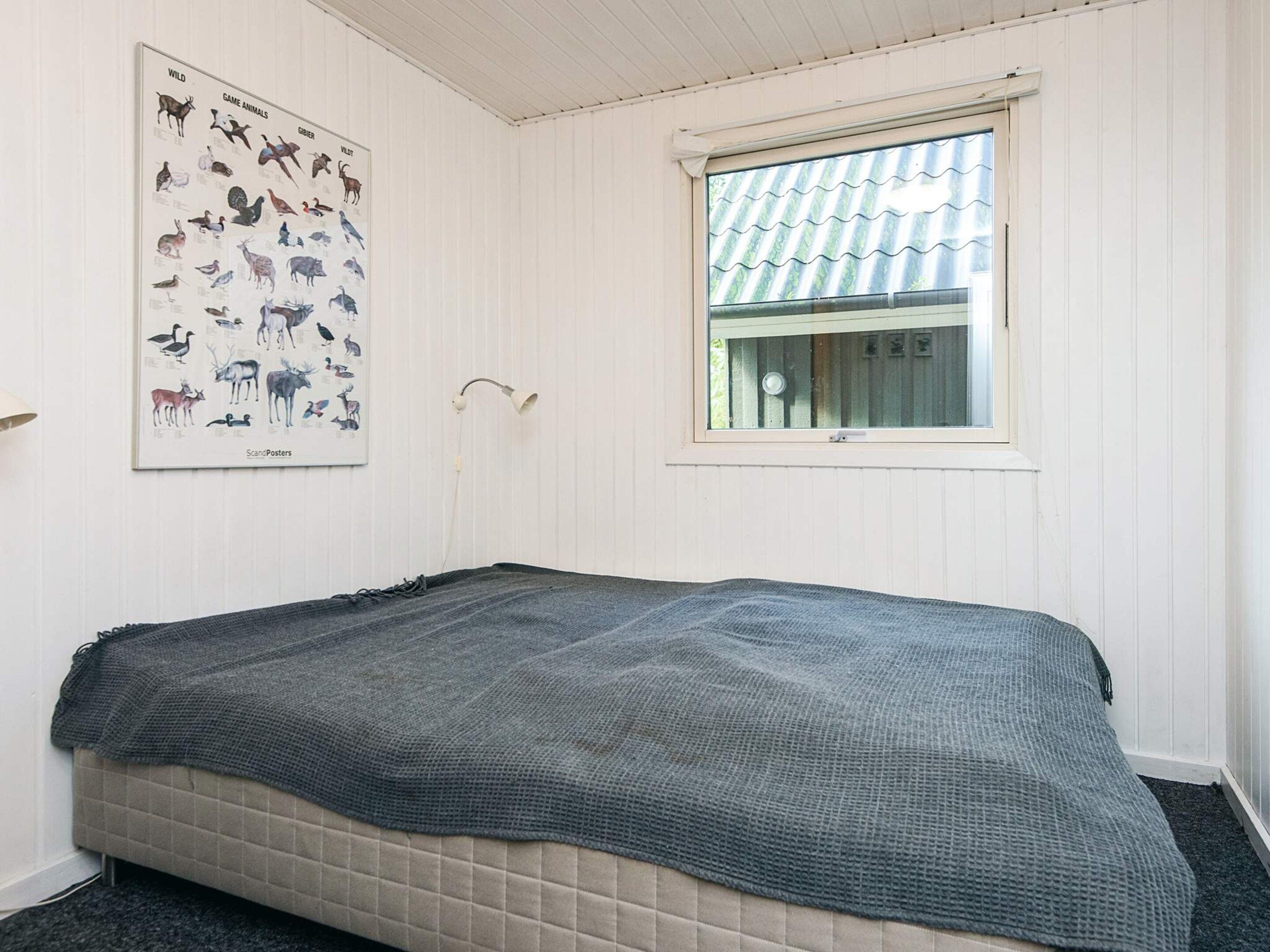 A bedroom with a bed, a window, and a poster on the wall.