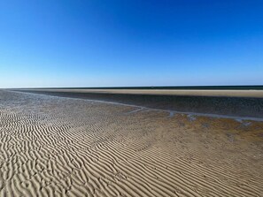 En strand med vågformade sandmönster och en klarblå himmel.