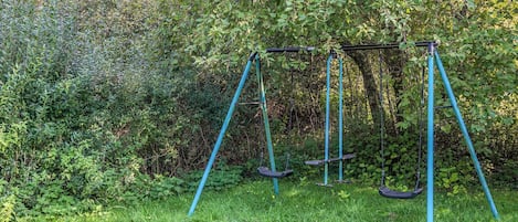 A swing set in a grassy area with dense foliage in the background.