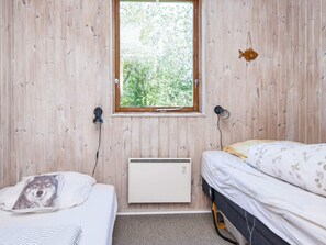 A small, wooden-paneled room with two beds, a window with a view of greenery, and a wall-mounted heater.