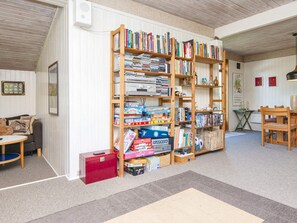 A room with a large bookshelf filled with books and games, a red storage box, a wooden table, and a chair.