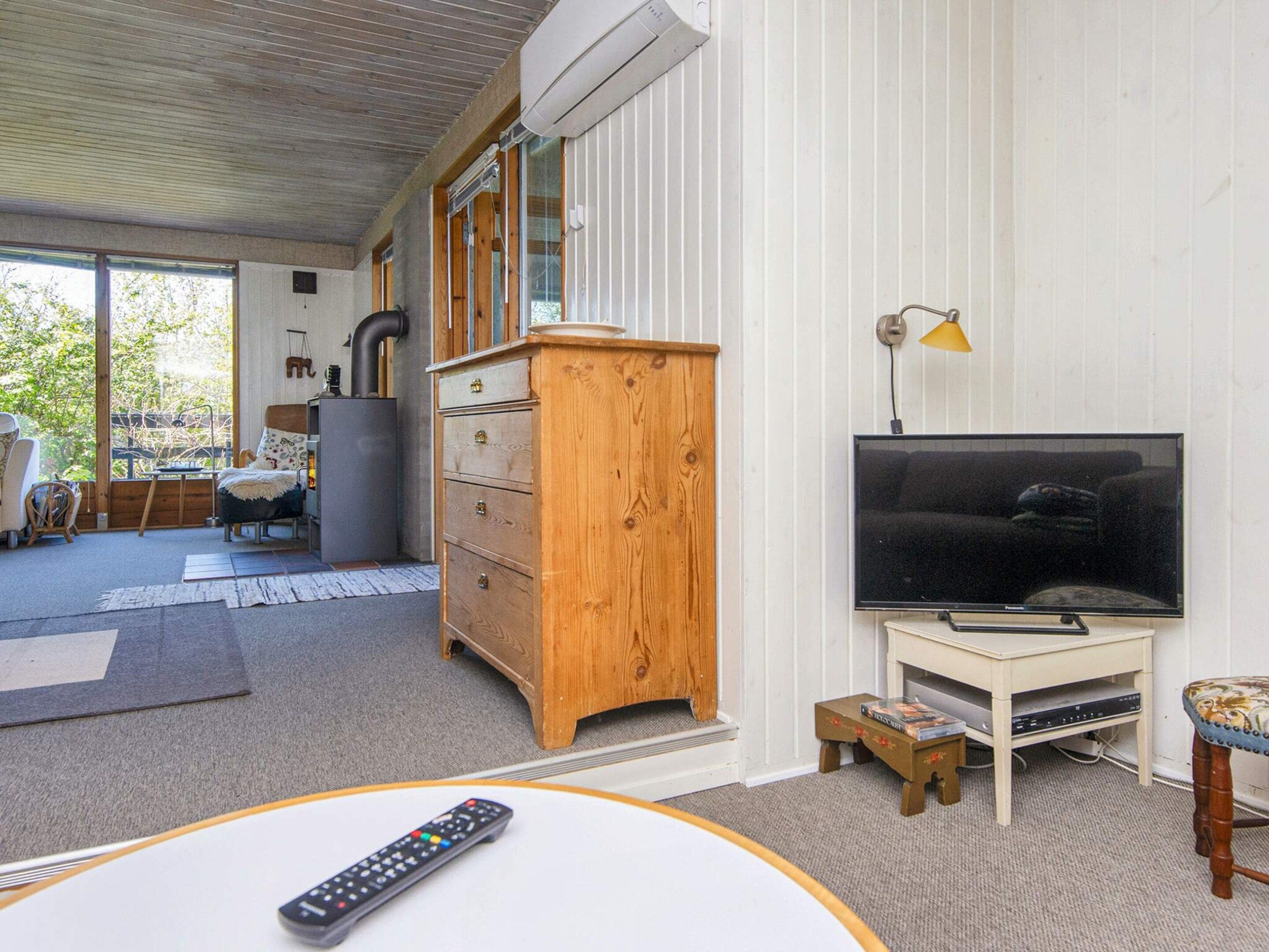 Uma sala de estar com televisão, um armário de madeira, um sofá e um espaço de jantar com mesa e cadeiras.