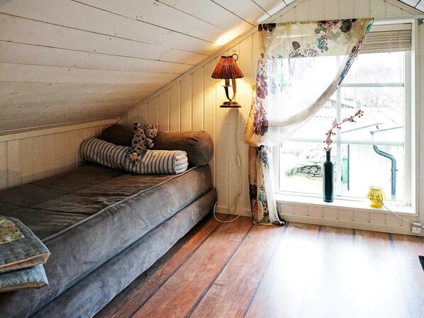 Ett mysigt sovrum på vinden med en säng, en lampa och ett fönster med gardiner.
