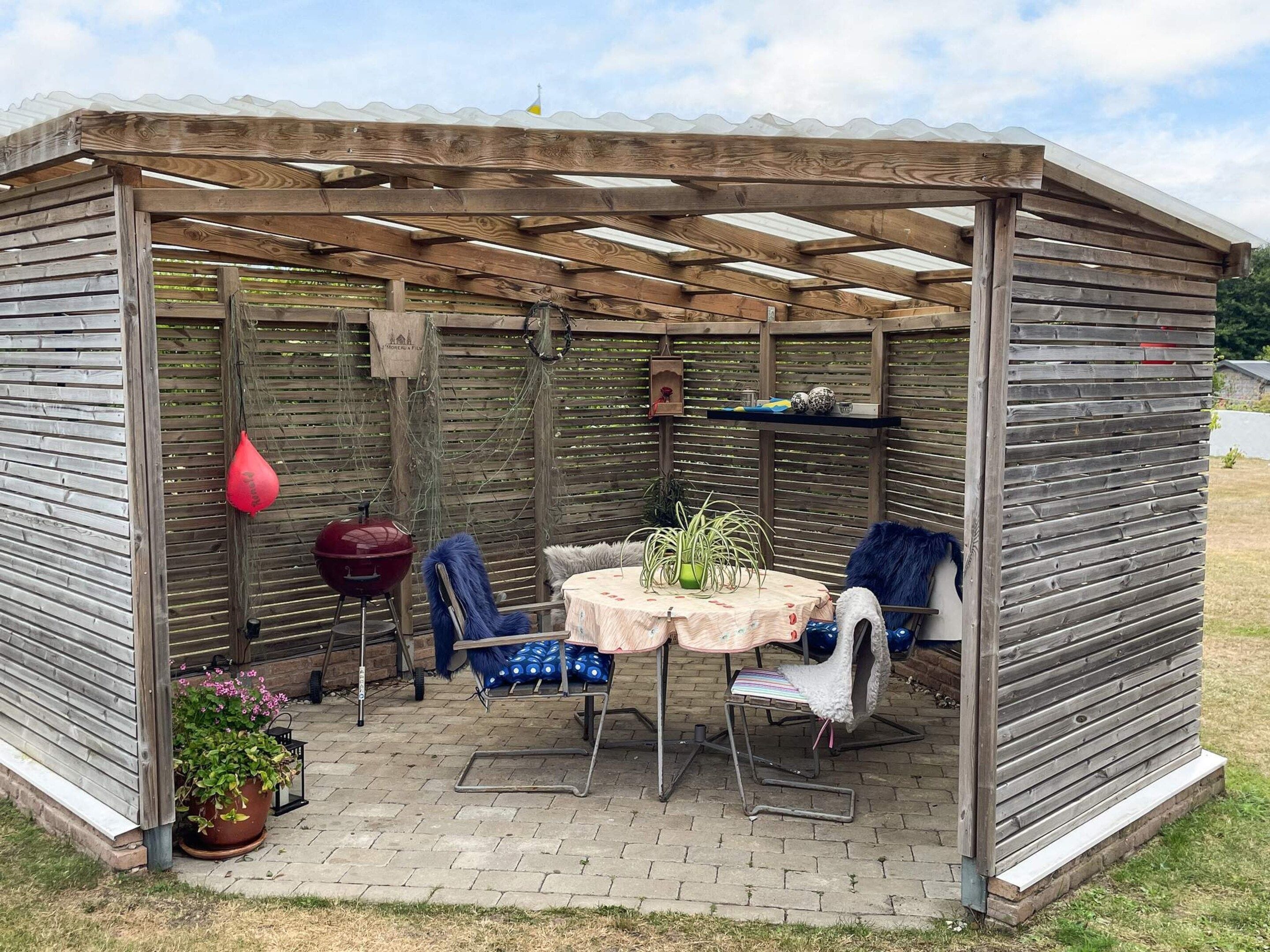 A covered patio area with a table and chairs, a grill, and potted plants.