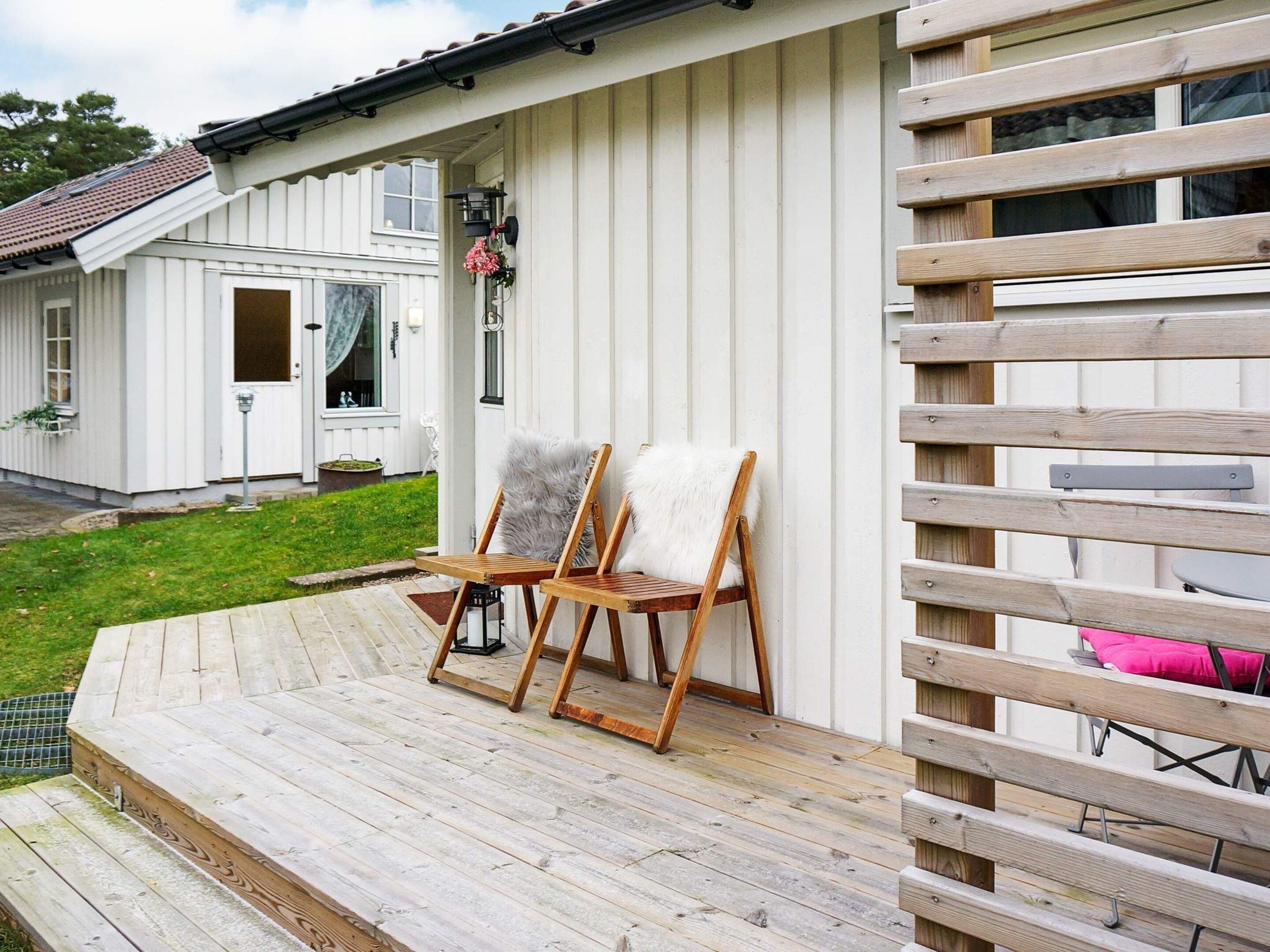 A wooden deck with two chairs and a small table, a white building with a door and windows, and a wooden fence.