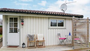 A small, single-story building with a tiled roof, a satellite dish, a door with a window, and a small porch area with two chairs and a table. - Holiday Home in Fängersfors (Falkenberg)