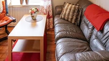 A living room with a leather sofa, a wooden table, and a red rug.