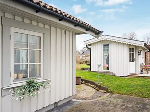 A white building with a window, a planter with greenery, and a paved area with a stone border.