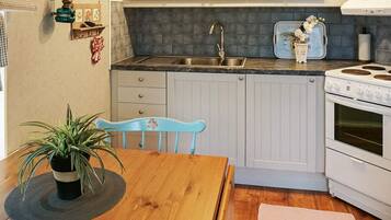 A compact kitchen with white cabinets, a stainless steel sink, a white stove, and a blue chair.