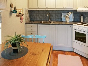 A compact kitchen with white cabinets, a stainless steel sink, a white stove, and a blue chair.