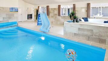 Una piscina interior con tobogán, un jacuzzi y una zona de estar con vistas al exterior.