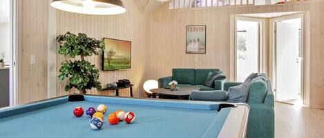 A pool table with balls, a sofa, a hanging light fixture, and a painting on the wall.