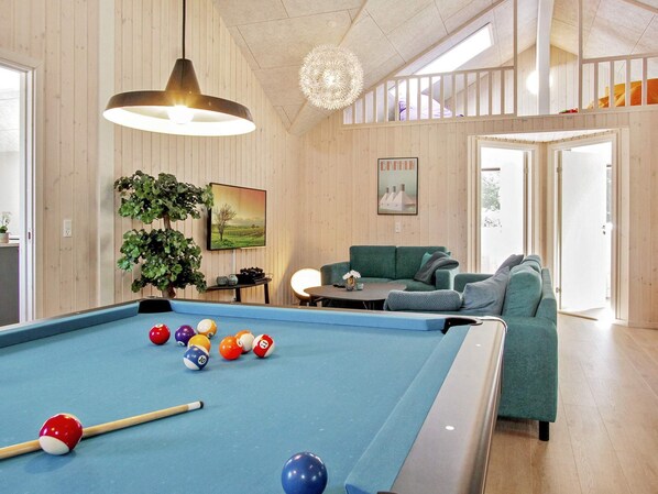 A pool table with balls, a sofa, a hanging light fixture, and a painting on the wall.