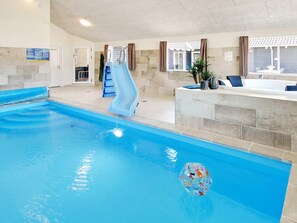 An indoor swimming pool with a slide, a hot tub, and a seating area.