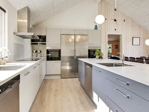A modern kitchen with stainless steel appliances, a dishwasher, and a dining area with chairs and a table. - 5 Star Holiday Home in Frederiksvaerk (Frederiksvaerk)
