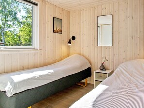 A room with two beds, a window, a wall-mounted lamp, and a small bedside table with a vase.