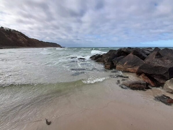 A beach with waves, rocks, and a cloudy sky.