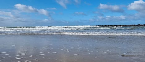 Una playa con olas, cielo despejado y una costa rocosa distante.