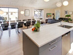 Una cocina moderna con una isla central, sillas negras y una zona de comedor con mesas y sillas.