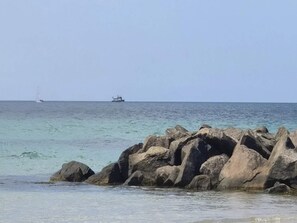 A rocky shoreline with calm sea and a distant ship.