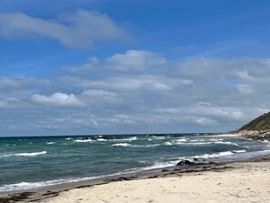 A beach with waves, a clear sky, and a rocky cliff. - 5 Star Holiday Home in Frederiksvaerk (Frederiksvaerk)