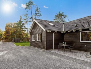 A wooden cabin with a sloped roof, a gravel driveway, and a patio with a table and chairs. - 5 Star Holiday Home in Frederiksvaerk (Frederiksvaerk)