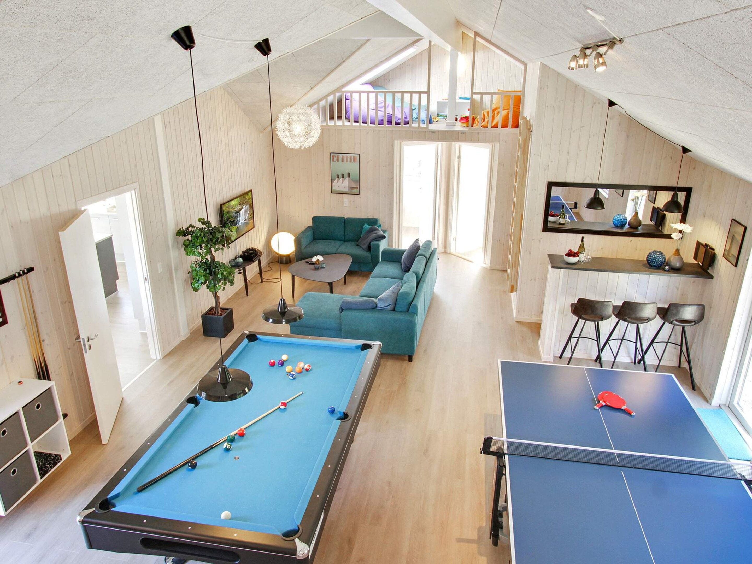 A spacious living area with a pool table, a sofa set, a dining area with bar stools, and a kitchen in the background.
