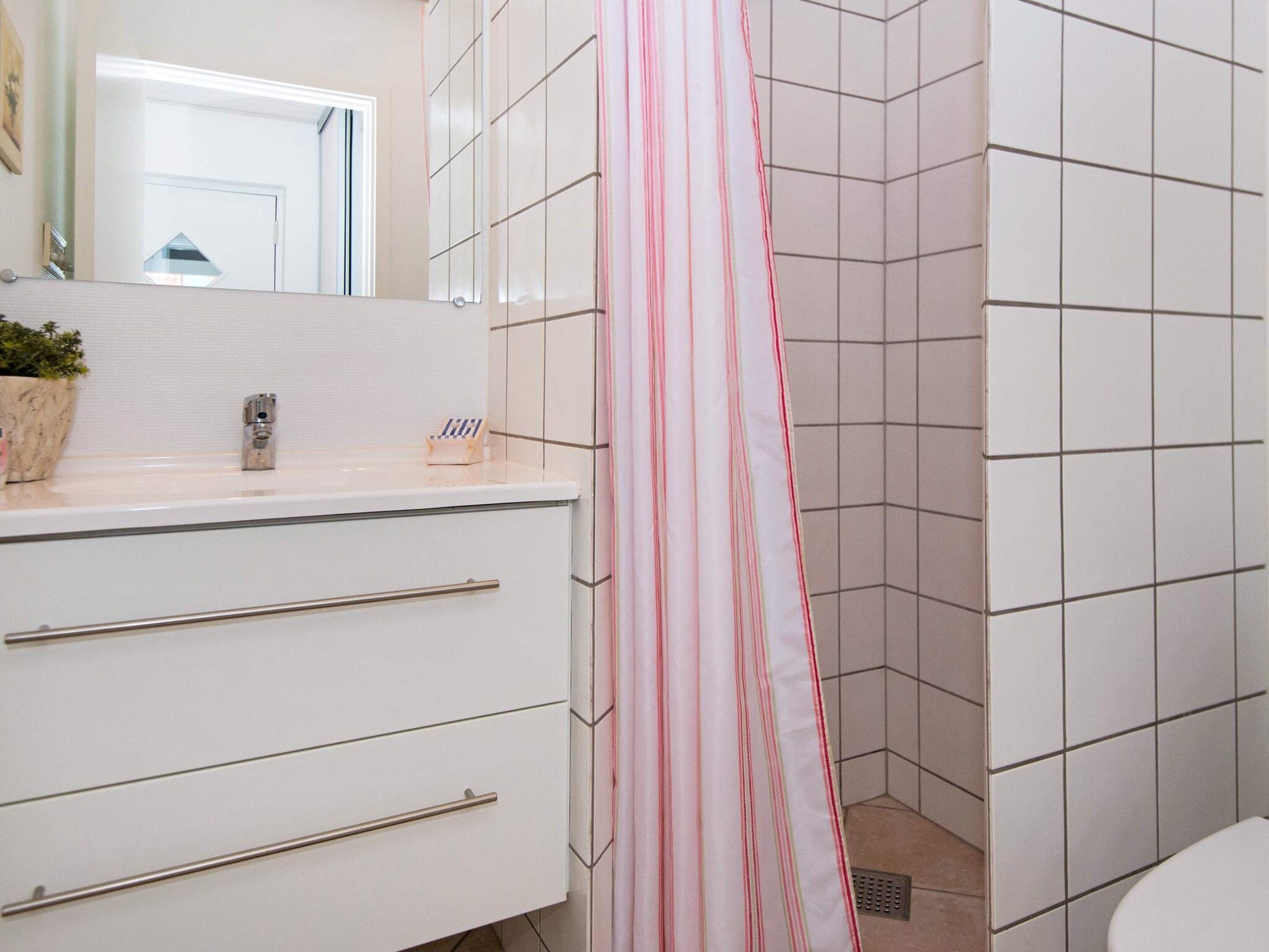 A bathroom with white tiles, a white sink with a mirror, and a shower curtain.