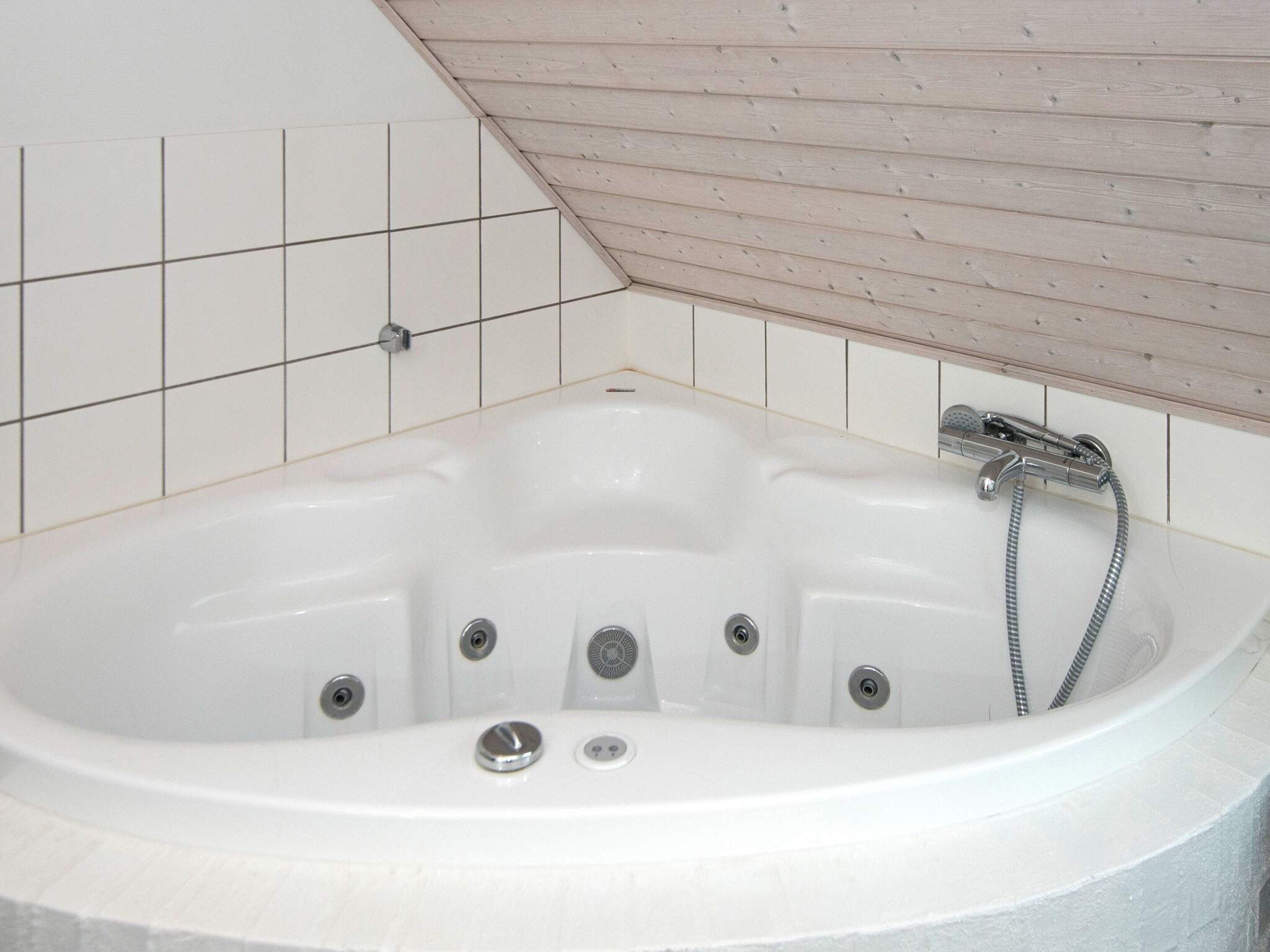 Un bagno con una vasca da bagno bianca, pareti piastrellate e un soffitto in legno.