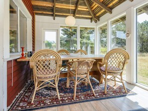 A dining area with a wooden table and wicker chairs, large windows, and a hanging light fixture.