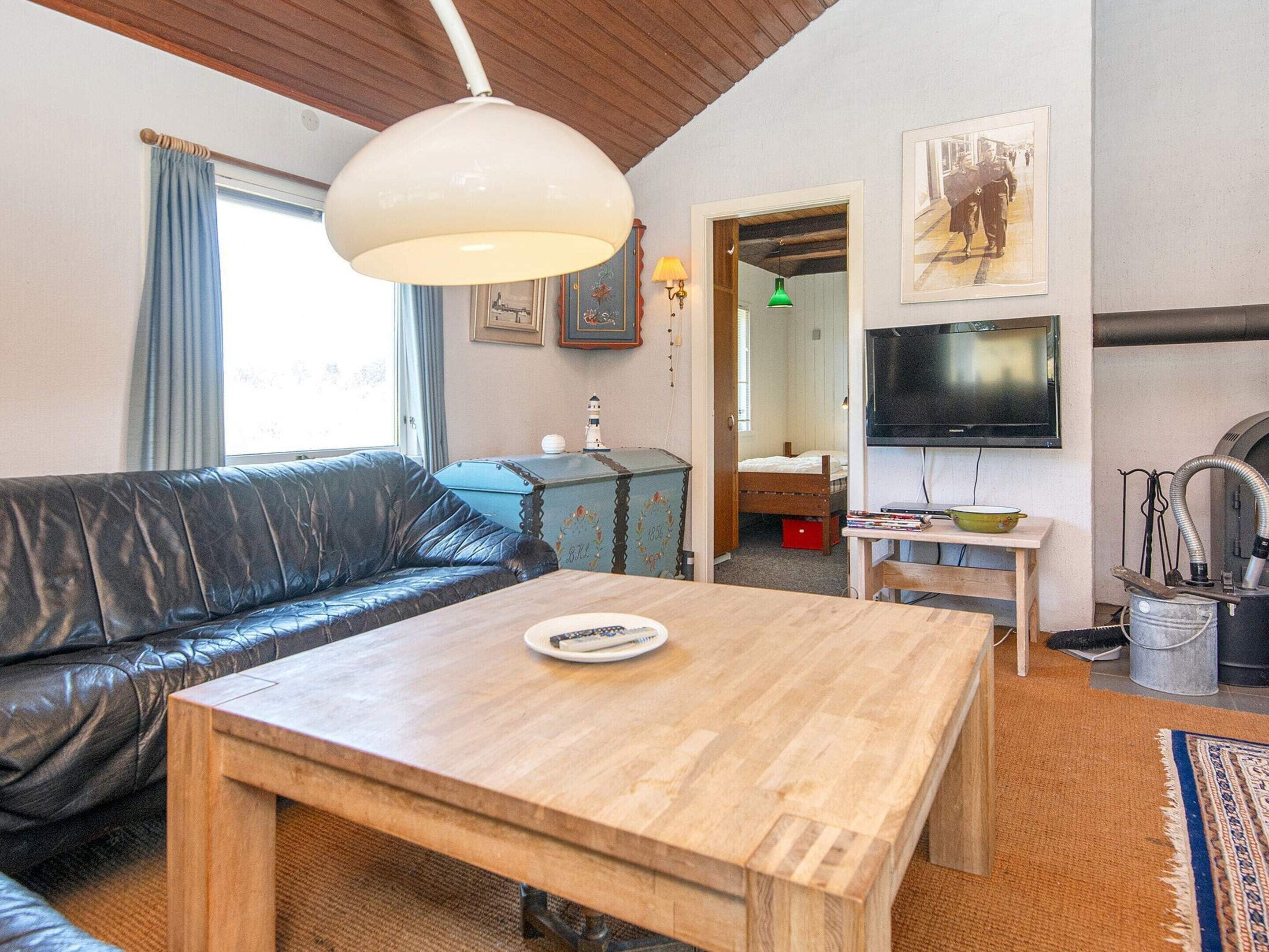 A cozy living room with a leather sofa, a wooden coffee table, a television, and a vintage suitcase.